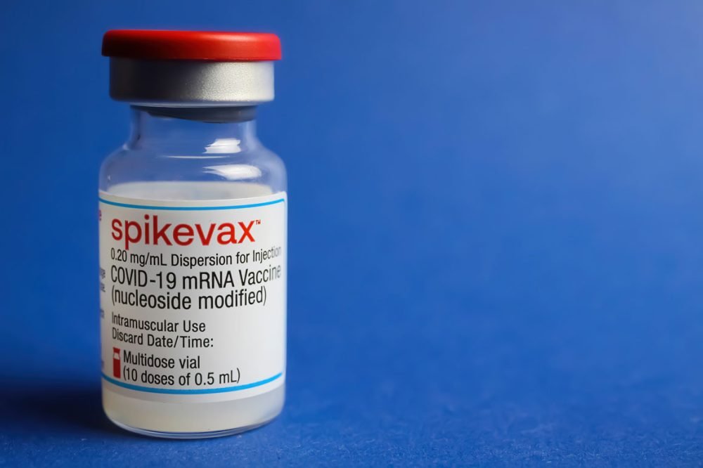 Frasco da vacina contra covid Spikevax sobre fundo azul.